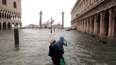 Una mujer sostiene a una niña mientras camina en una inundada plaza de San Marcos. Reuters / Manuel Silvestri