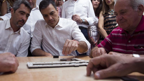 El líder del PSOE y candidato a la presidencia del Gobierno, Pedro Sánchez (c), coloca su ficha en una partida de dominó que ha jugado hoy con los mayores del Centro de Participación Activa de Anica Torres de Benalmádena (Málaga), junto al 