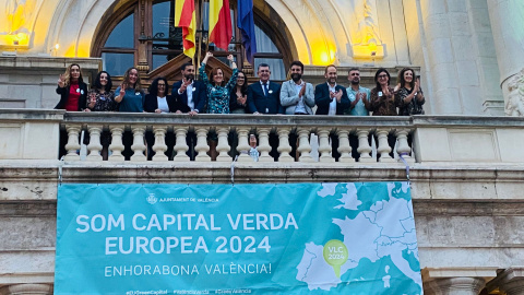 Parte de la corporación municipal de València saluda desde el balcón del Ayuntamiento con un cartel donde indica que la ciudad será la Capital Europea Verde 2024.