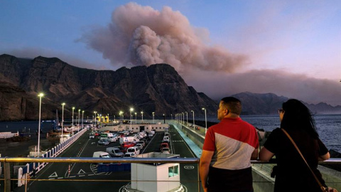 Dos personas observan al caer la tarde la columna de humo reactivada en el Pinar de Tamadaba que se ve desde el muelle de Agaete. EFE/Ángel Medina G.