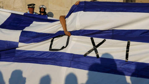 Los manifestantes sostienen una bandera griega junto a agentes de la policía antidisturbios en frente del edificio del Parlamento durante una manifestación contra la austeridad y por el 'NO' en el referéndum en Atenas.- REUTERS / Yannis Beh