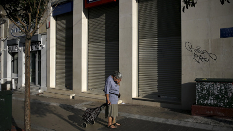 Una mujer que tira de un carrito de la compra se detiene frente a sucursal de Eurobank cerrada en Atenas, Grecia, tras declararse el control de capitales.  -REUTERS / Alkis Konstantinidis