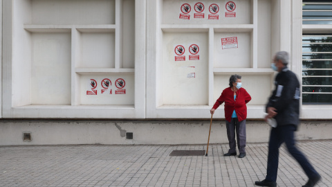 Dos personas mayores con mascarilla delante del Centro de Salud Pavones, donde hay carteles de protesta que rezan 'Urgencias Cerradas, tu salud vendida', a 21 de octubre de 2022, en Madrid.