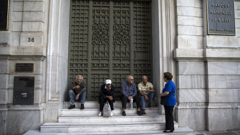 La gente se sienta en la puerta de una sucursal del Banco Nacional de Grecia, cerrado tras el corralito por el anuncio del referedum sobre las medidas propuestas por los acreedores de la deuda griega.- REUTERS / Marko Djurica