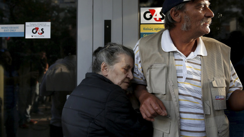 Vallia (L), un jubilado de 75 años de edad, de Atenas, se aferra a la puerta de una sucursal del Banco Nacional de Grecia con la esperanza de obtener su pensión, junto a otros jubilados en Atenas, tras establecerse el control de capitales e