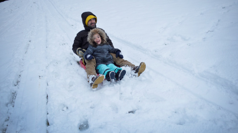 Padre e hija tirándose en trineo después de la nevada en el puerto vasco de montaña de Urkiola. / Reuters