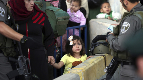 Una niña palestina mira al soldado israelí que revisa las identificaciones de las mujeres palestinas que quieren cruzar el paso de control de Belén, al sur de Jerusalén. EFE