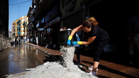 Dos ciudadanas vacían cubos de granizo en la calle después de la tormenta y la granizada que cayó este lunes en esta localidad causando importantes daños materiales.- EFE