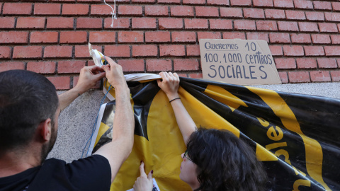 Dos jóvenes cuelgan una pancarta en la puerta de La Ingobernable.- EUROPA PRESS