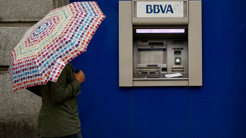 Una mujer con paraguas junto a un cajero automático de una sucursal de BBVA en Madrid. REUTERS/Andrea Comas