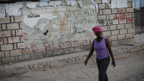 Una mujer pasa frente a un cartel de Oxfam en Corail, campamento para desplazados a las afueras de Puerto Príncipe, Haití. / Reuters