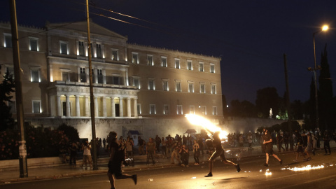 Un manifestante lanza a la policía un cóctel molotov a la policía frente al edificio del Parlamento, en plena Plaza Syntagma. EFE/YANNIS KOLESIDIS