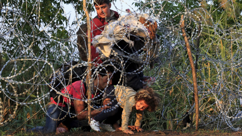 Una niña junto a su familia, refugiados sirios, trata de cruzar la valla de cuchillas instalada por Hungría en su frontera con Serbia, cerca Röszke.- REUTERS / Bernadett Szabo