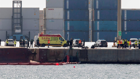 Efectivos de la Guardia Civil y del servicio de emergencias esperan en el Muelle del Centenario de Port Castelló durante las tareas de búsqueda de dos personas desaparecidas tras el vuelco del buque "Nazmuye Ana" (a la izquierda, en la imag