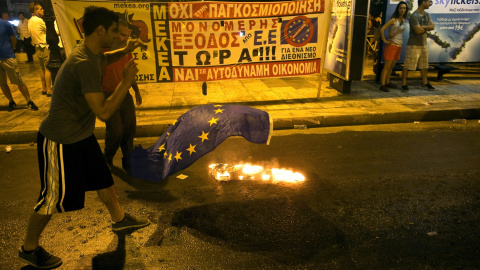 An anti-austerity demonstrator throws a European Union flag into a fire in front of the parliament in Athens, Greece July 22, 2015. Greek Prime Minister Alexis Tsipras sought on Wednesday to contain a rebellion in his left-wing Syriza party