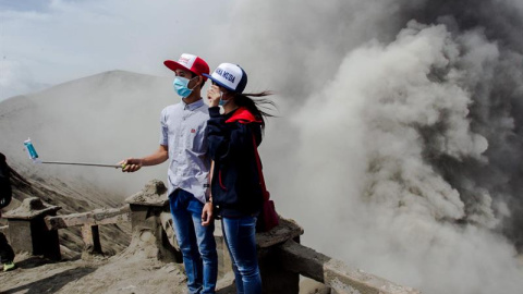 Dos jóvenes posan para un selfie mientras el volcán Bromo arroja cenizas al aire durante una erupción volcánica en Probolinggo, Indonesia. EFE/Fully Handoko