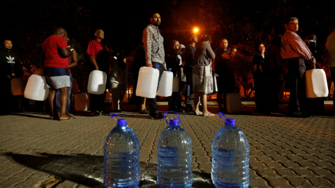 Varios ciudadanos hacen cola para recoger agua de una fuente en uno de los suburbios de Ciudad del Cabo. REUTERS