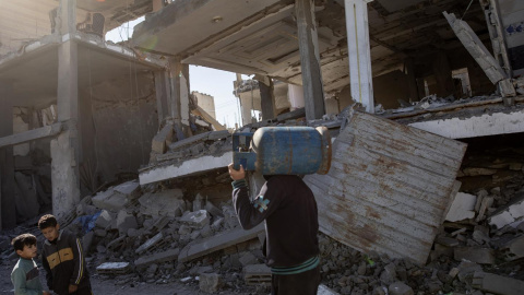 Un palestino que lleva una bombona de gas al hombro pasa junto a los escombros de un edificio residencial destruido en el campo de refugiados de Rafah, al sur de la Franja de Gaza, el 4 de febrero de 2024.