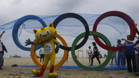 Vinicius, la mascota de los Juegos de Río, posa junto a la escultura de los anillos olímpicos. - EFE