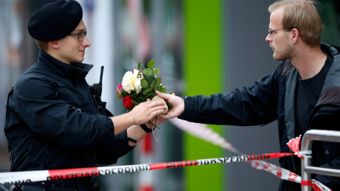 Un hombre entrega un ramo de flores a uno de los policías que custodian el lugar del tiroteo. - REUTERS