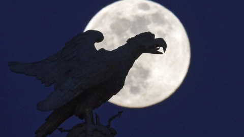 Una estatua con forma de águila en el castillo Sanssouci silueteada frente a la luna llena en Postdam, Alemania. EFE/Ralf Hirschberger