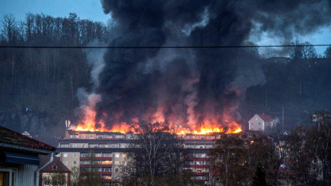 Varios bomberos intentan contener las llamas tras declararse un incendio en un complejo residencial en Huskvarna, en el sur de Suecia. El fuego se propagó rápidamente por el los áticos que obligó a 160 residentes a abandonar rápidamente sus