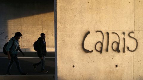 Varios inmigrantes caminan tras un muro en el que está escrito Calais, cerca de las instalaciones del eurotúnel que comunica Francia con Inglaterra. crisis. REUTERS/Pascal Rossignol