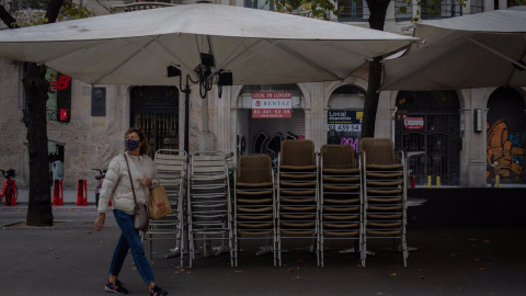 Una mujer pasa junto a la terraza recogida de un bar cerrado.