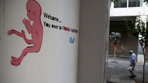 Una pintada en una calle de Atenas de un dibujo de un recién nacido con una frase que dice:  "Bienvenido ... le debes a la Troika 36.730 €". REUTERS / Alkis Konstantinidis