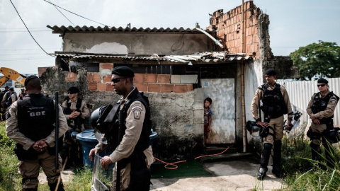 Un niño se asoma, en presencia de la Policía, por la puerta de su casa después de que la de sus vecinos fuera demolida en el barrio de Vila Autódromo, en Río de Janeiro. - AFP