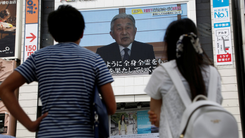 Un par de personas observan en una pantalla en la calle en Tokio el mensaje del emperador Akijito. REUTERS/Kim Kyung-Hoon