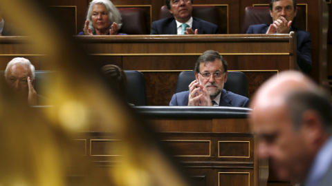 El presidente del Gobierno, Mariano Rajoy, observa al ministro de Economía, Luis de Guindos, durante su intervención en el pleno del Congreso.- REUTERS