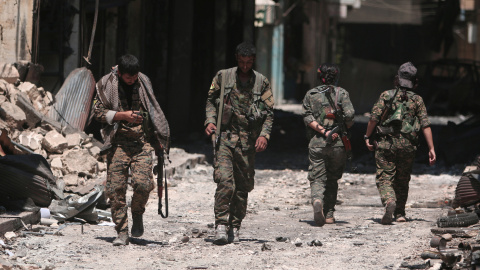 Combatientes de las Fuerzas Democráticas de Siria (SDF) caminan sobre los escombros de tiendas y edificios dañados en la ciudad de Manbij, en Alepo, Siria. REUTERS / Rodi Said