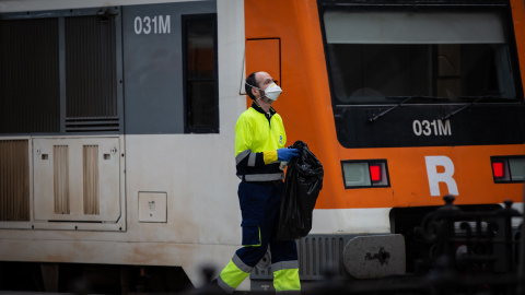 Un trabajador de la limpieza trabaja protegido con una mascarilla junto a un tren en Barcelona/Catalunya (España)