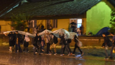 Los migrantes se protegen de la lluvia con un plástico mientras caminan para coger el tren en dirección a la frontera con Serbia, después de recibir el permiso para cruzar en Macedonia en la estación de tren en Gevgelija.-EFE