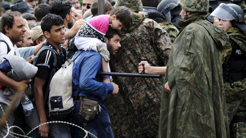 Un policía amenaza con la porra a una refugiado sirio que quiere cruzar la frontera de Grecia a Macedonia.- REUTERS/Ognen Teofilovski