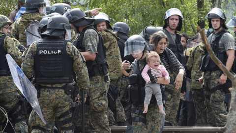 Una policía ayuda a cruzar el cordón a una refugiada y a su hija, en la frontera entre Grecia y Macedonia.-EPA/GEORGI LICOVSKI