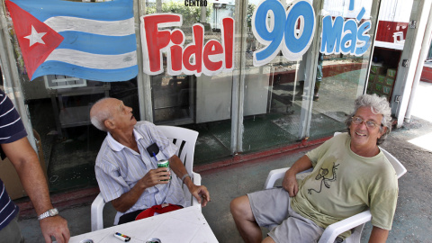 Unas personas toman cerveza junto a un anuncio alusivo al 90 cumpleaños del líder de la revolución cubana Fidel Castro. EFE/Ernesto Mastrascusa