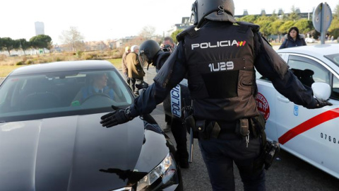 Efectivos de la Policía Nacional entre un vehículo de licencia VTC y un taxi a las puertas del recinto ferial de Ifema. EFE/Chema Moya