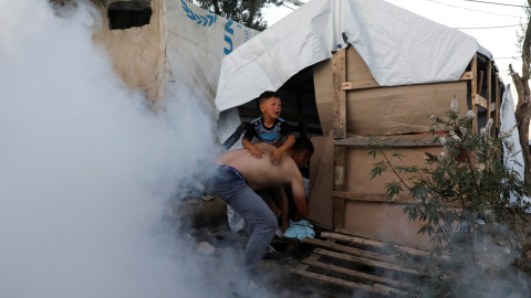 Un migrante coge a un niño mientras huyen de gases lacrimógenos disparados por la policía antidisturbios durante una manifestación, después de un incendio en el campamento de Moria en la isla de Lesbos. REUTERS/Giorgos Moutafis