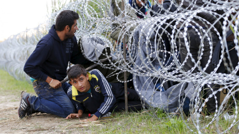 Refugiados sirios cruzan debajo de una alambrada con cuchillas e la frontera entre Hungría y Serbia, cerca Röszke.- REUTERS / Laszlo Balogh