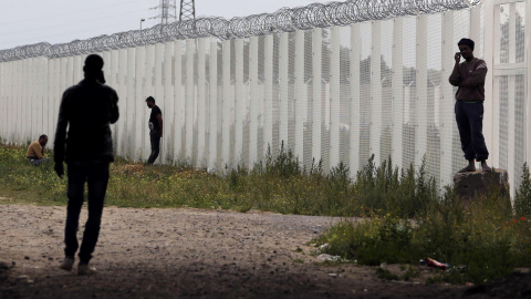 Varios inmigrantes llaman por teléfono cerca de una cerca con alambre de púas, junto al campamento improvisado llamado "La nueva jungla" en Calais, Francia.- REUTERS / Regis Duvignau