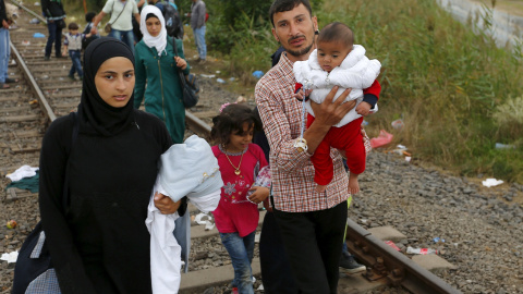 Refugiados sirios caminan con sus hijos en brazos a lo largo de una vía de ferrocarril, después de cruzar la frontera húngaro-serbio en Hungría, cerca Röszke, donde se ha construído una alambrada de cuchillas para frenarlos de 175 km de lon