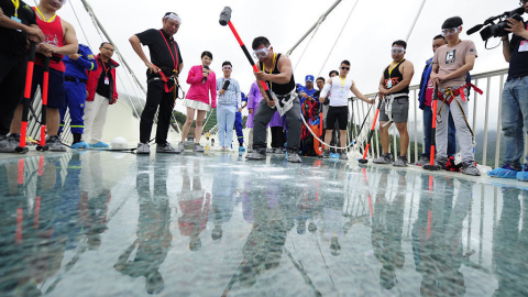 Un visitante golpea el suelo de cristal del puente con un martillo en una prueba de seguridad. Visual China Group