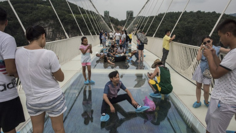 Un visitante posa para una foto sobre el suelo de cristal del puente más largo y más alto del mundo sobre el valle del parque natural de Zhangjiajie, en la provincia china de Hunan. AFP/FRED DUFOUR