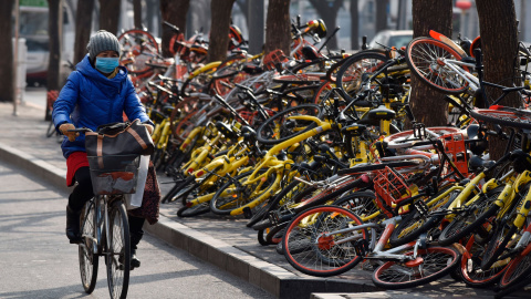 Una mujer pasa junto a varias bicicletas compartidas tiradas en el suelo en una carretera en Pekín. China ha emitido pautas nacionales que rigen las operaciones de bicicletas compartidas en 2017 en un esfuerzo por nutrir una nueva industria