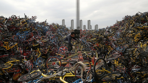 Un trabajador desenreda una cuerda en medio de miles de bicicletas apiladas en un lote en Xiamen, provincia de Fujian, China. A medida que algunas de las empresas crecieron demasiado en muy poco tiempo fueron quebrando y se retiraron, por l