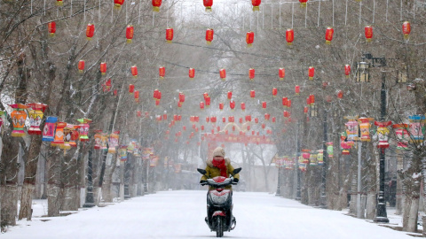 Una mujer conduce una motocicleta y pasa por una calle cubierta de nieve decorada con faroles, antes del Año Nuevo Lunar Chino, en Zhangye, Gansu | Reuters