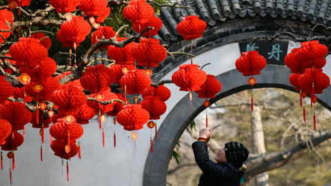 Una mujer usa su teléfono móvil para tomar una foto de las linternas rojas antes del Año Nuevo Lunar Chino en un parque en Beijing | AFP/ Wang Zao