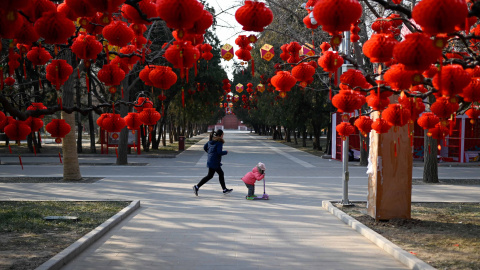 Una niña corre con un niño de pie en un scooter pasando linternas rojas antes del Año Nuevo Lunar Chino en un parque en Beijing | AFP/ Wang Zao